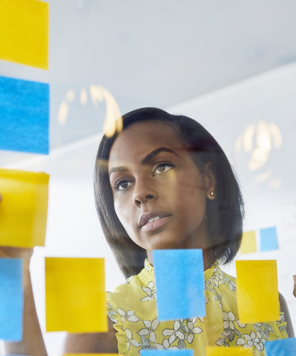 Young woman in office, sticking sticky notes to glass in office